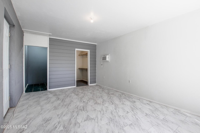 unfurnished bedroom featuring a walk in closet, marble finish floor, a closet, a wall mounted air conditioner, and baseboards