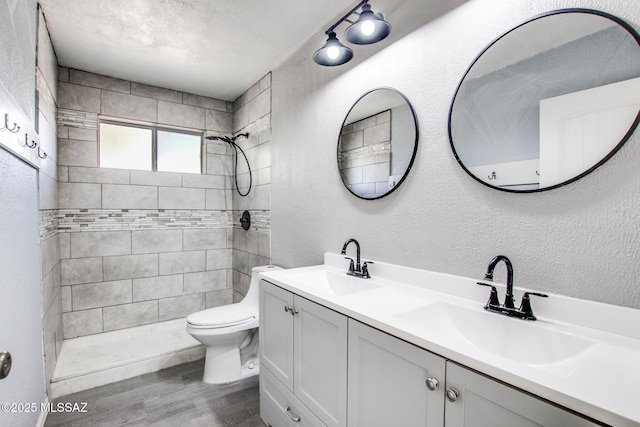 full bathroom featuring wood finished floors, tiled shower, a sink, and toilet