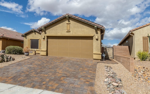 view of front of house with a garage, a tile roof, decorative driveway, a gate, and stucco siding