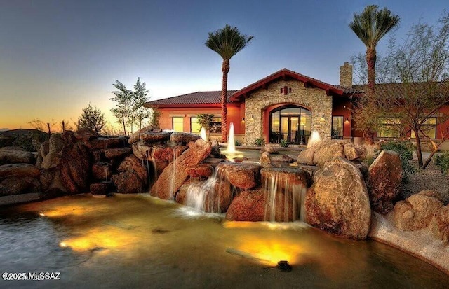 exterior space with stone siding, french doors, a chimney, and a tiled roof