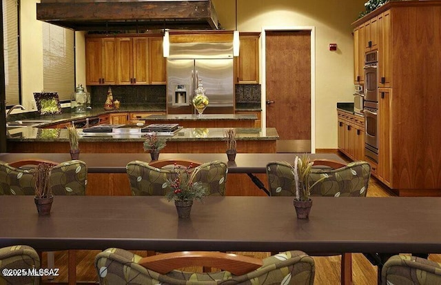 kitchen featuring brown cabinets, dark countertops, backsplash, appliances with stainless steel finishes, and a sink