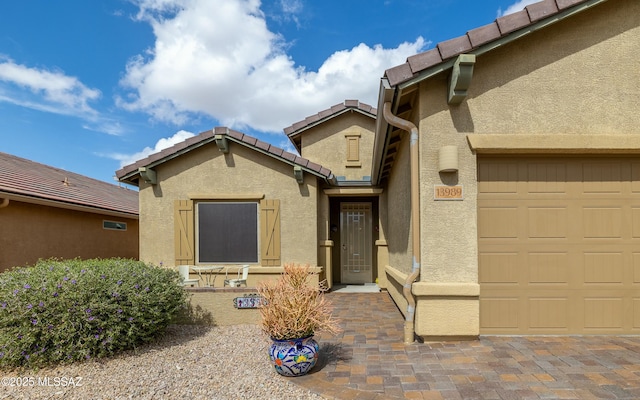 entrance to property featuring a tile roof, an attached garage, and stucco siding