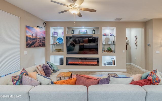 living area with ceiling fan, built in shelves, a glass covered fireplace, and visible vents