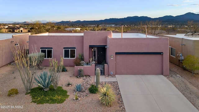 pueblo-style house featuring an attached garage, fence, a mountain view, and stucco siding