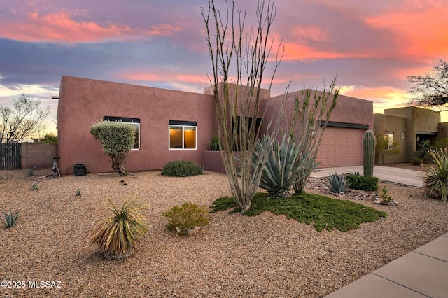 adobe home with an attached garage, fence, driveway, and stucco siding