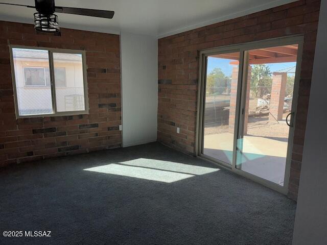 carpeted spare room with brick wall and a ceiling fan