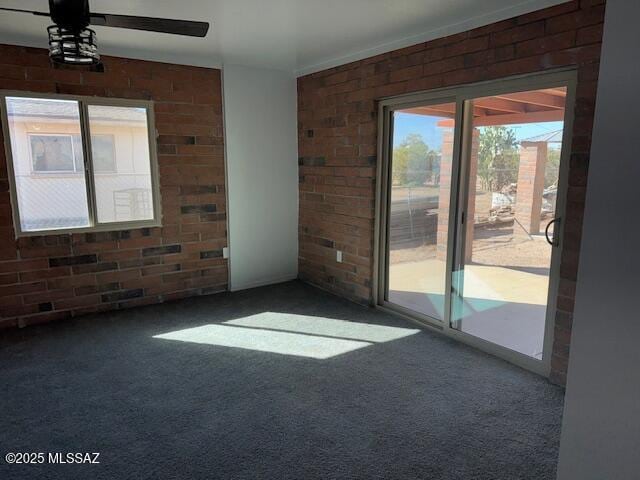 carpeted empty room featuring a ceiling fan and brick wall