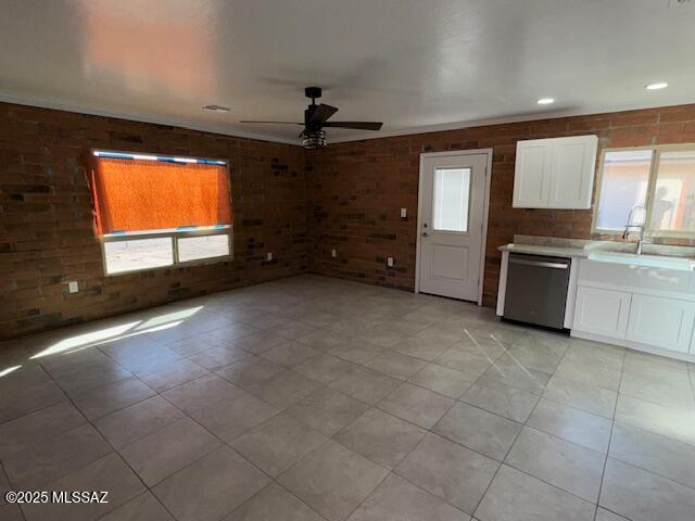 kitchen featuring brick wall, a sink, white cabinetry, a ceiling fan, and stainless steel dishwasher