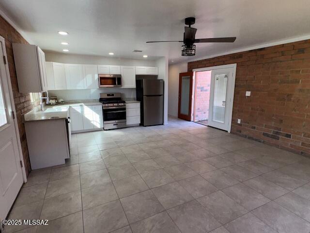 kitchen with stainless steel appliances, light countertops, white cabinets, ceiling fan, and brick wall