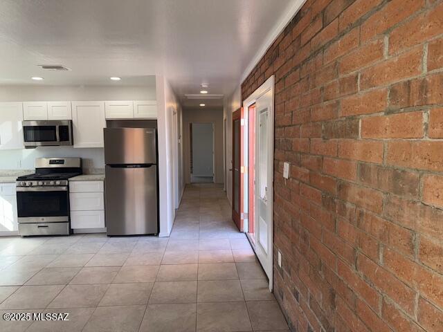 kitchen featuring white cabinetry, brick wall, visible vents, and appliances with stainless steel finishes