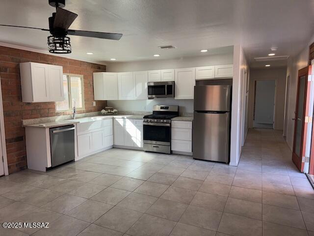 kitchen with visible vents, ceiling fan, brick wall, stainless steel appliances, and white cabinetry