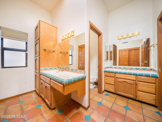 bathroom with tasteful backsplash, baseboards, toilet, two vanities, and a high ceiling