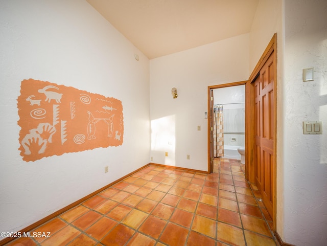 empty room featuring lofted ceiling, light tile patterned floors, and baseboards