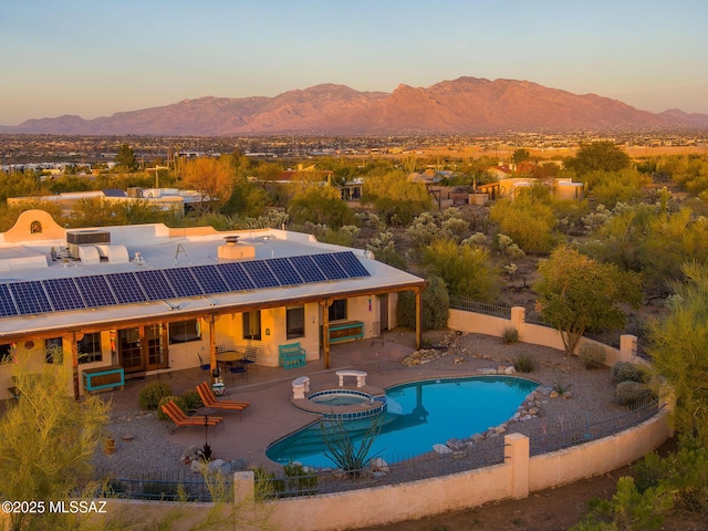 pool at dusk with a patio, a fenced backyard, a mountain view, and a pool with connected hot tub