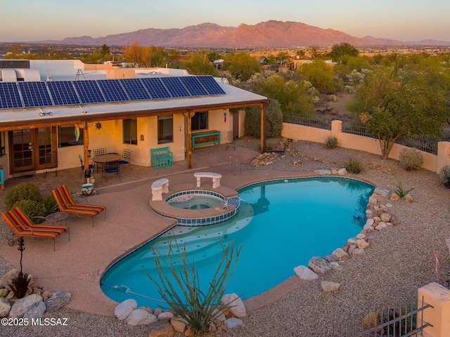 pool at dusk featuring a patio area, a fenced backyard, a mountain view, and a pool with connected hot tub