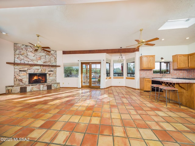 unfurnished living room featuring light tile patterned flooring, a stone fireplace, a skylight, and a ceiling fan