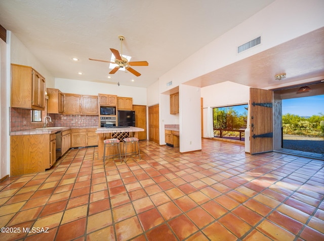 kitchen with visible vents, decorative backsplash, black appliances, a kitchen breakfast bar, and open floor plan