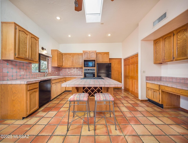 kitchen featuring a skylight, visible vents, tile countertops, and black appliances