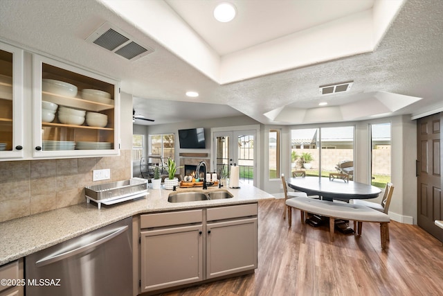 kitchen featuring visible vents, a tray ceiling, a peninsula, a sink, and stainless steel dishwasher