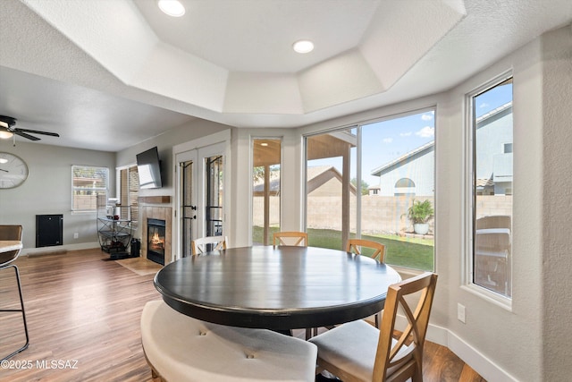 dining room with wood finished floors, baseboards, a fireplace, ceiling fan, and a raised ceiling