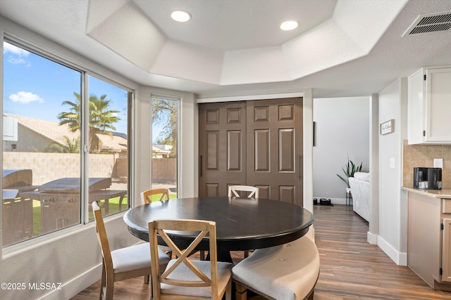 dining room featuring a tray ceiling, wood finished floors, visible vents, and baseboards