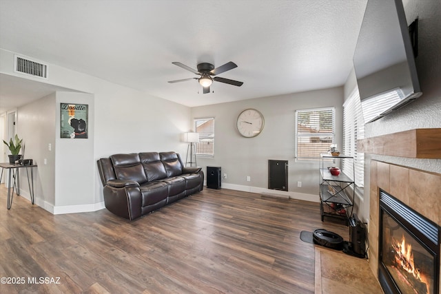 living room with visible vents, a tile fireplace, baseboards, and wood finished floors