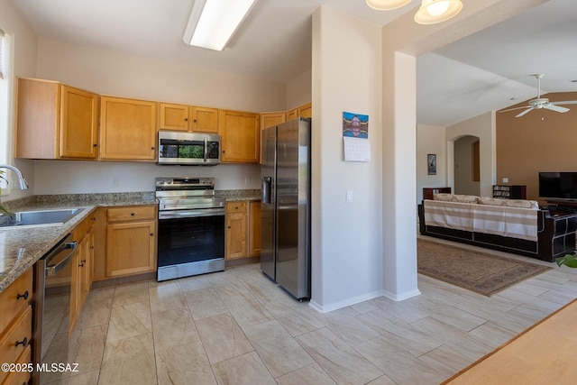 kitchen featuring arched walkways, light stone counters, open floor plan, stainless steel appliances, and a sink