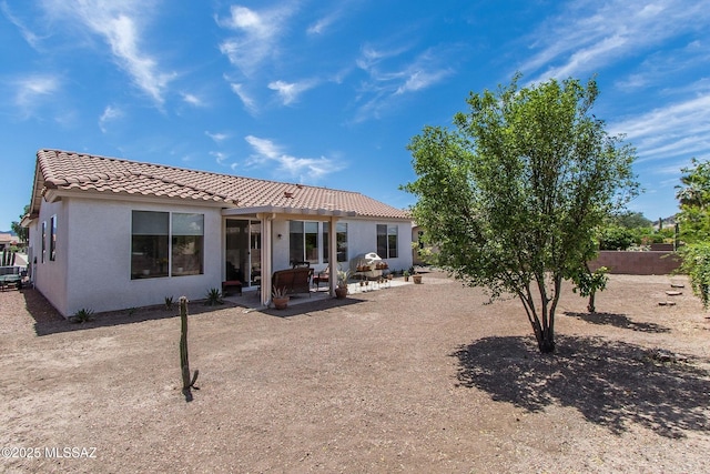 rear view of property featuring fence, a patio, a tiled roof, and stucco siding