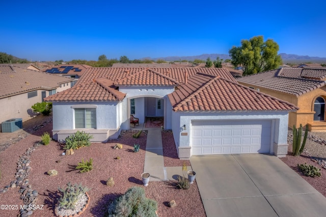 mediterranean / spanish home featuring a garage, cooling unit, concrete driveway, and stucco siding