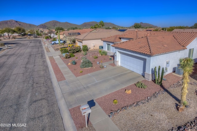 view of front facade with a tile roof, central air condition unit, concrete driveway, an attached garage, and a mountain view