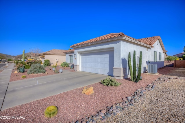 mediterranean / spanish-style home featuring central air condition unit, stucco siding, a garage, driveway, and a tiled roof