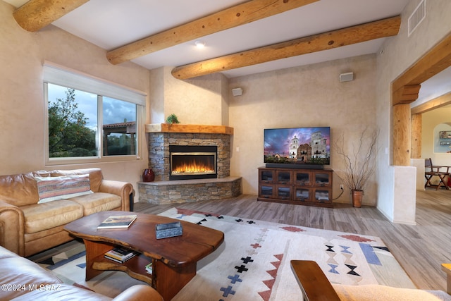 living room with visible vents, beamed ceiling, a stone fireplace, and wood finished floors