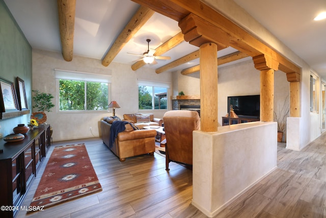 living room with ceiling fan, a stone fireplace, wood finished floors, and beam ceiling