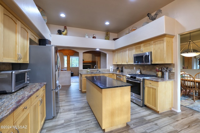 kitchen with light brown cabinets, stainless steel appliances, a sink, and a center island