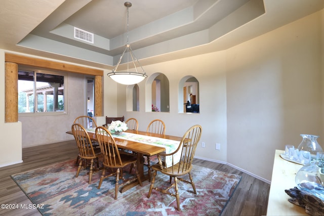 dining area with a tray ceiling, visible vents, baseboards, and wood finished floors