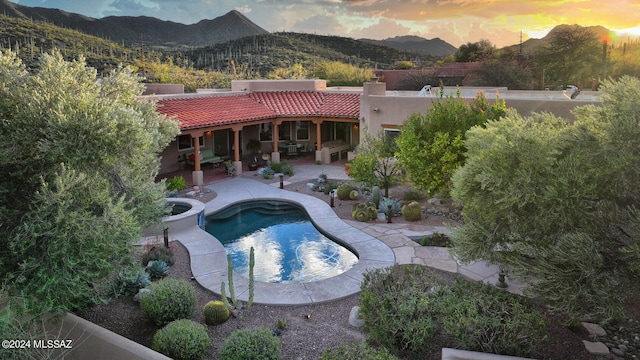 back of property at dusk featuring a patio, a mountain view, a tiled roof, stucco siding, and a chimney