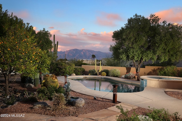 pool at dusk with a fenced in pool, a patio, a fenced backyard, an in ground hot tub, and a mountain view