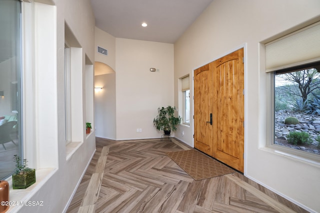 foyer entrance with arched walkways, visible vents, baseboards, and recessed lighting