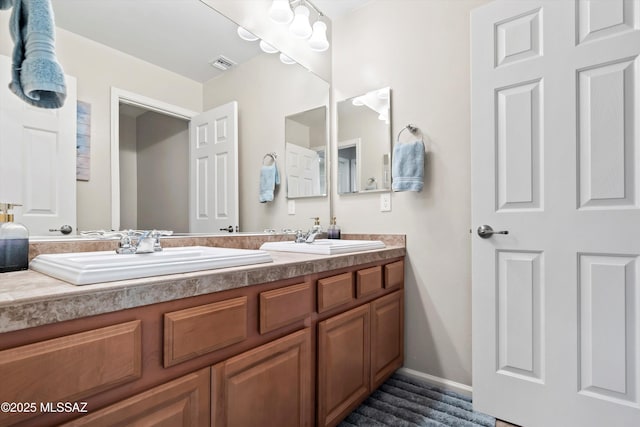 bathroom with double vanity, baseboards, visible vents, and a sink