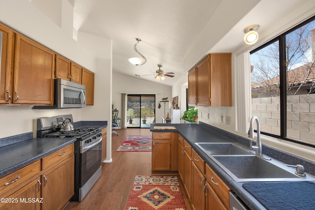 kitchen featuring dark wood finished floors, dark countertops, appliances with stainless steel finishes, vaulted ceiling, and a sink