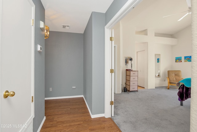 hallway featuring carpet floors, wood finished floors, visible vents, and baseboards