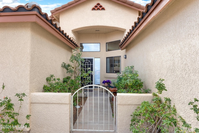 doorway to property featuring a tile roof, a gate, and stucco siding