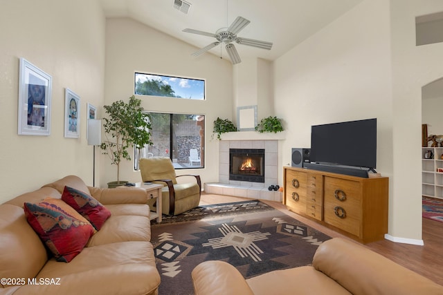 living room with visible vents, a ceiling fan, wood finished floors, high vaulted ceiling, and a tile fireplace