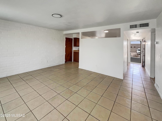 unfurnished room featuring light tile patterned floors, brick wall, and visible vents