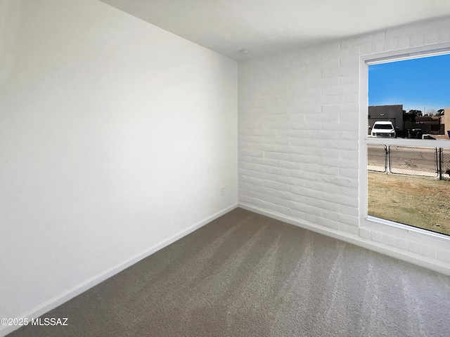 unfurnished room with brick wall, baseboards, and dark colored carpet