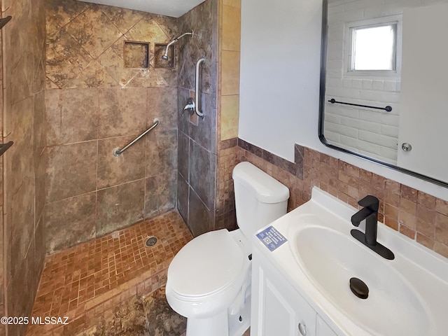 bathroom with a tile shower, tile walls, toilet, and vanity