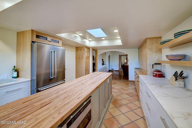 kitchen with butcher block countertops, a skylight, appliances with stainless steel finishes, arched walkways, and open shelves