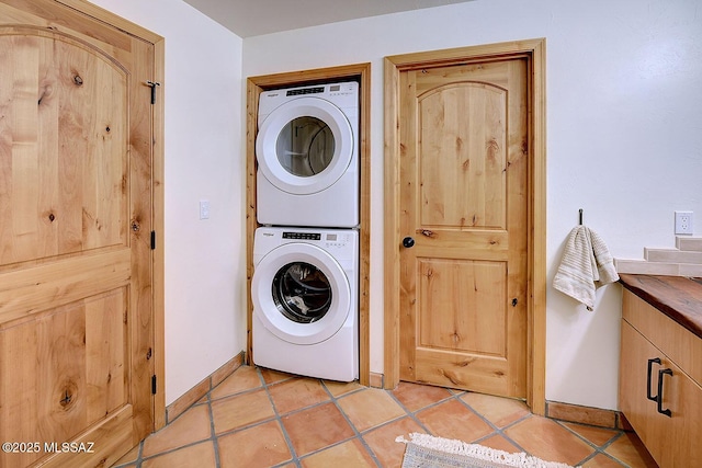clothes washing area with stacked washer / dryer, light tile patterned floors, baseboards, and laundry area