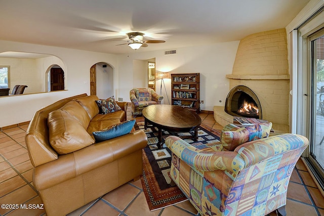tiled living area with a fireplace, visible vents, arched walkways, and ceiling fan