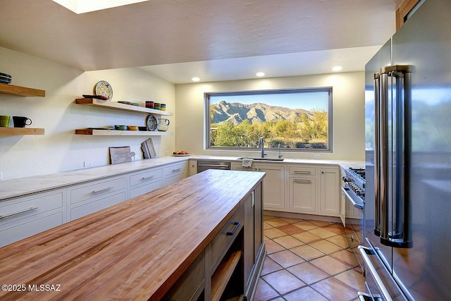 kitchen featuring open shelves, a sink, butcher block counters, white cabinets, and high quality fridge